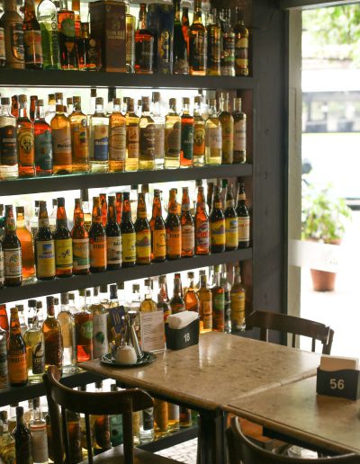 Indoor setting of Academia da Cachaça in Barra, with shelves filled with neatly organized cachaça bottles and small tables in front. Natural light enters through the window, creating a cozy atmosphere.