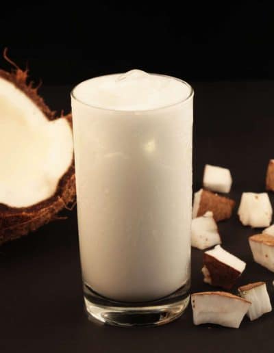 Batida de coco em copo, com pedaços de coco fresco ao redor.