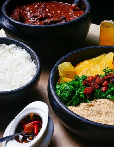 Academia's Feijoada served with rice, collard greens, orange, farofa, and house-made pepper sauce - traditional Brazilian dish.